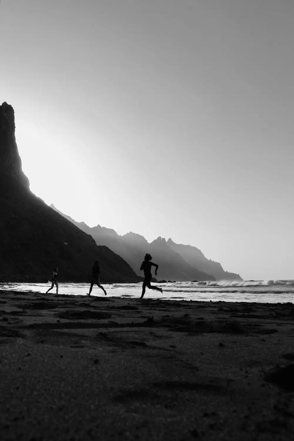 Trois coureurs en silhouette sur une plage, au pied d'une falaise, à l'aube